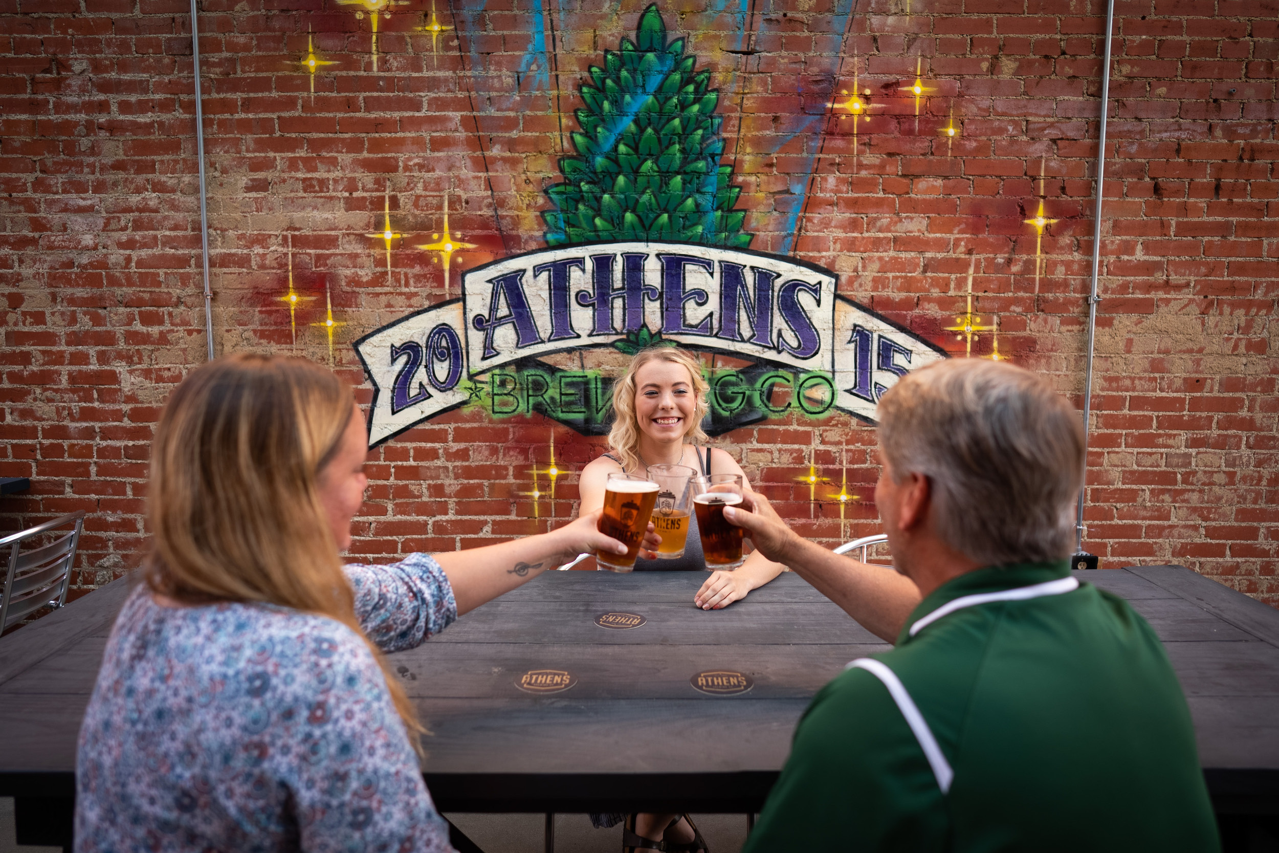 Three people touching their Athens Brewing glasses at a table